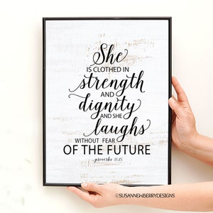 May include: A framed print with a white background and black text that reads "She is clothed in strength and dignity and she laughs without fear of the future - Proverbs 31:25".
