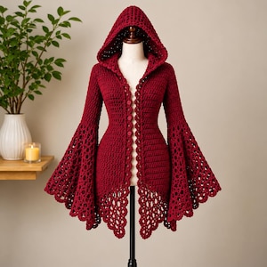 May include: A deep red crochet cardigan featuring a pointed hood, long sleeves with wide flared cuffs, and a front button closure. The garment displays a dense stitch pattern on the bodice and an intricate openwork lace design on the sleeves and hem.