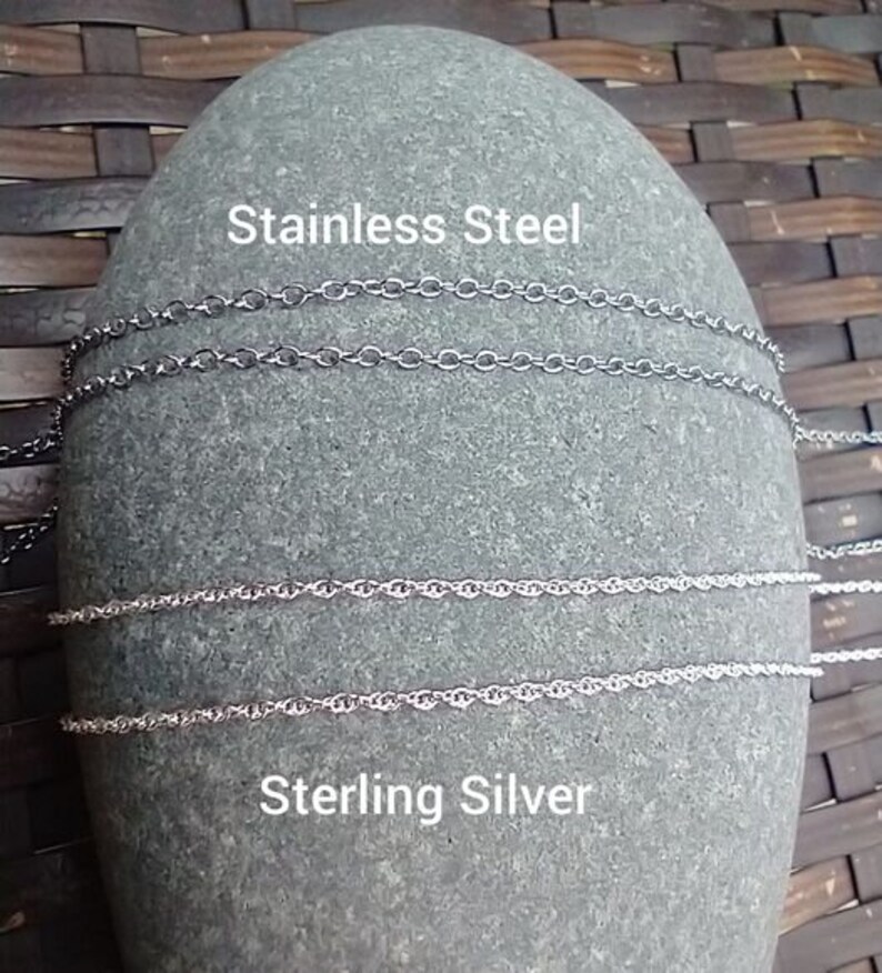 May include: Close-up of a gray stone with two silver chains and two stainless steel chains. The text "Stainless Steel" and "Sterling Silver" is printed on the stone.