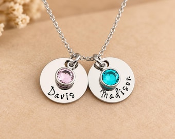 May include: A silver-toned necklace featuring two circular metal charms suspended from a delicate chain. Each charm is engraved with a name, Davis and Madison, and is set with a single round faceted gemstone, one light pink and one teal blue.