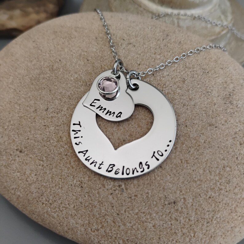 May include: Silver necklace with a heart pendant that says "This Aunt Belongs To..." and a smaller heart pendant with the name "Emma" and a pink rhinestone.