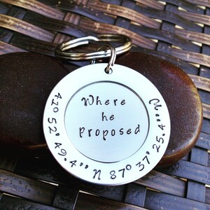 May include: A silver keychain with a round tag that says "Where he proposed" and coordinates engraved around the edge. The coordinates are 41° 52' 49.4" N 87° 31' 25.4" W.