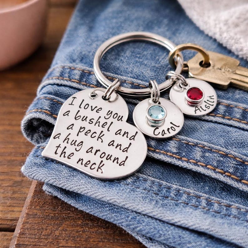 May include: A silver keychain with a heart-shaped charm engraved with the phrase "I love you a bushel and a peck and a hug around the neck." It includes two round charms with names and gemstones, and a key.