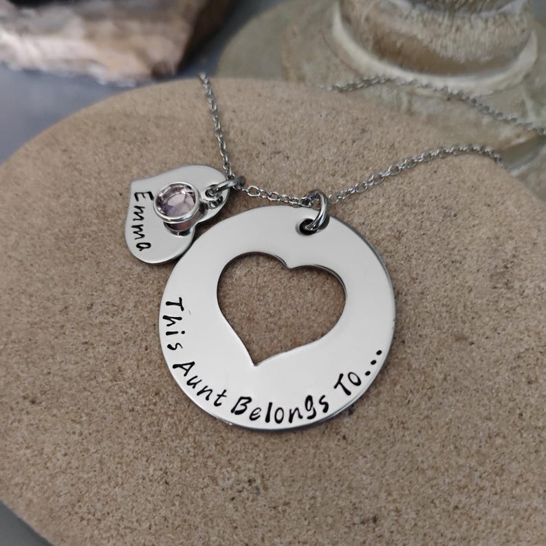 May include: Silver necklace with a heart-shaped pendant that says "This Aunt Belongs To..." and a smaller heart pendant with a pink rhinestone that says "Emma".