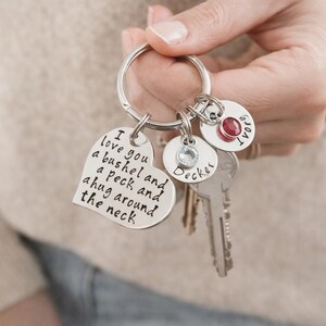 May include: A silver keychain with multiple charms. One heart-shaped charm has the text "I love you a bushel and a peck and a hug around the neck." Other charms include a round charm with a red gem and the name "Decker".