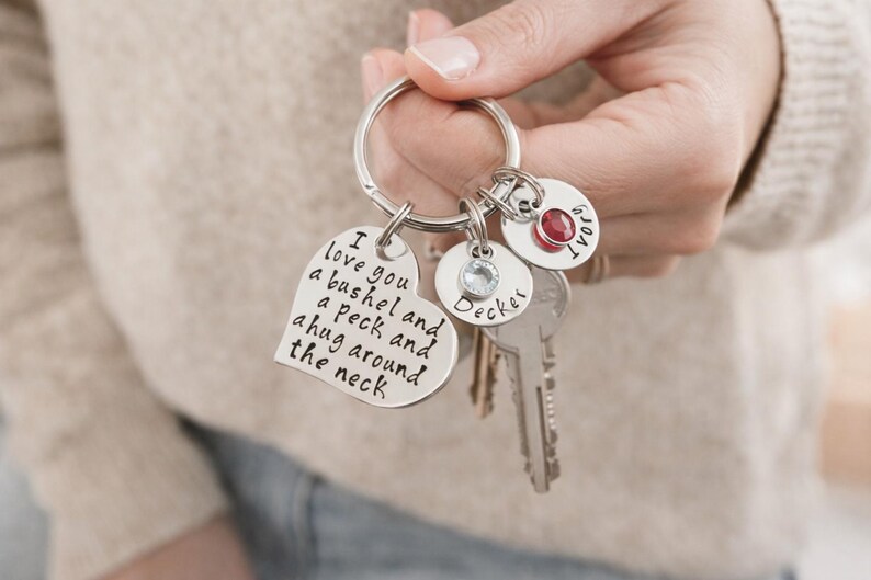 May include: A silver keychain with multiple charms. One heart-shaped charm has the text "I love you a bushel and a peck and a hug around the neck." Other charms include a round charm with a red gem and the name "Decker".