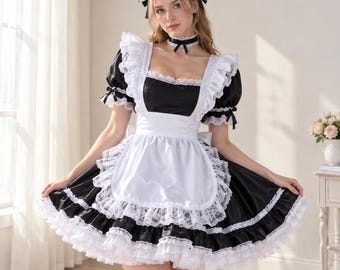 Op de afbeelding: Een zwart-witte dienstmeisjesjurk met een vierkante halslijn, korte pofmouwen en een wit schort met kanten rand. De outfit bevat een bijpassend kanten hoofdbandje, een choker met een strik en witte dijhoge kousen met zwarte strikjes.
