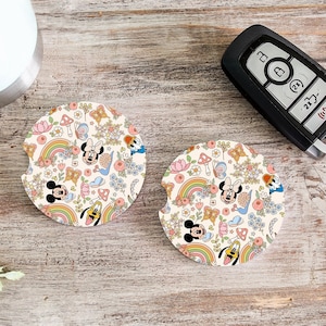 May include: Two round white coasters with a colorful pattern of Mickey Mouse, Minnie Mouse, and Goofy characters. The pattern includes rainbows, flowers, butterflies, and stars.