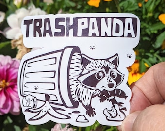 May include: A white sticker with the text "Trashpanda" in black lettering. A black and white illustration of a raccoon peeking out of a trash can is below the text.