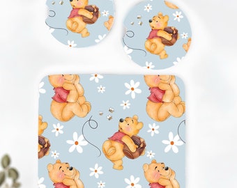May include: Set of three Winnie the Pooh coasters featuring a light blue background with white daisies and Winnie the Pooh holding a honey pot. The coasters are round and have a white border.