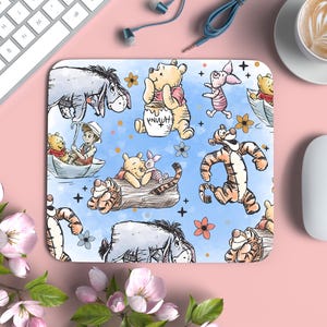 May include: Rectangular mousepad featuring a watercolor illustration of Winnie the Pooh and friends. The design includes characters like Pooh, Piglet, Tigger, and Eeyore on a light blue background with flowers and stars. A white keyboard and mouse are visible.
