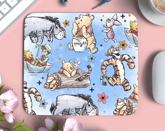 May include: Rectangular mousepad featuring a watercolor illustration of Winnie the Pooh and friends. The design includes characters like Pooh, Piglet, Tigger, and Eeyore on a light blue background with flowers and stars. A white keyboard and mouse are visible.