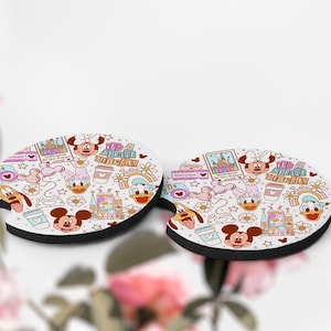 May include: Two white, oval-shaped car coasters with a black border. The coasters feature a repeating pattern of Disney characters, including Mickey Mouse, Minnie Mouse, Donald Duck, and Daisy Duck, along with the text "It's a small world!"