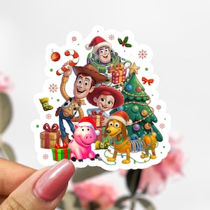 Peut inclure: Un autocollant coloré représentant les personnages de Toy Story célébrant Noël. Woody tient un sucre d'orge, Buzz l'Éclair porte un bonnet de Père Noël, et Jessie, Hamm et Zigzag sont également présents. Un sapin de Noël et des cadeaux complètent la scène festive.