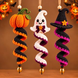 May include: Three hanging crochet ornaments featuring a pumpkin with a green stem, a white ghost with a purple bow, and a black witch hat. Each ornament has a spiral tail in alternating colors, a wooden bead at the top, and a gold bell at the bottom.
