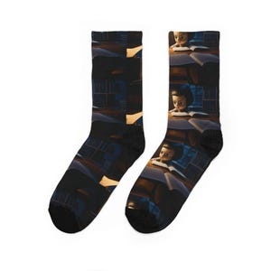 May include: A pair of crew socks featuring a repeating digital illustration of a child with dark hair reading a book in a dimly lit library. The scene is rendered in warm amber and deep blue tones, showing the child focused on an open book.