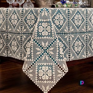 May include: An off-white, cream-coloured rectangular tablecloth featuring an intricate, repeating crochet pattern of diamond-shaped motifs and floral-inspired centres. The fabric has a delicate, open-work mesh design with scalloped edges.