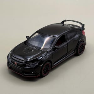 Può includere: Un modellino di auto Honda Civic Type R nero con finitura lucida, accenti rossi sulle ruote e sul paraurti anteriore, uno spoiler posteriore e interni dettagliati visibili attraverso i finestrini trasparenti. Dotato di presa d'aria sul cofano.