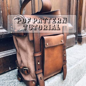 Può includere: Uno zaino in pelle marrone e tela con manico superiore, tasca frontale con patta e cinghie verticali in pelle con rivetti metallici. Il testo PDF PATTERN TUTORIAL è sovrapposto alla parte superiore dello zaino con un carattere scuro.