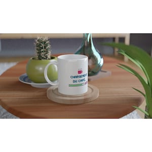 Könnte beinhalten: Ein weißer Keramikbecher mit einer verpixelten Grafik eines rosafarbenen Kaffeetassensymbols, dem blauen Text "CHARGEMENT DU CAFÉ..." und einem grünen Ladebalken, der 87% anzeigt. Der Becher hat einen geschwungenen Henkel und steht auf einem runden Holzuntersetzer.