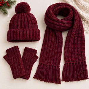 May include: A deep burgundy winter set consisting of a ribbed knit beanie with a matching pom-pom, a long ribbed scarf with fringed ends, and a pair of fingerless gloves. Each piece features a consistent vertical ribbed texture.