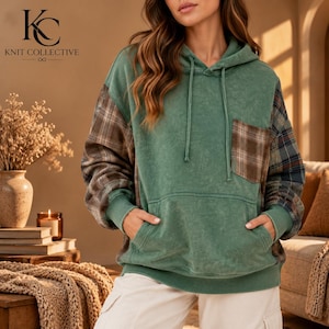 Puede incluir: Una sudadera con capucha verde con acabado desgastado, mangas largas de tela a cuadros marrones y azules, un bolsillo en el pecho a juego, un bolsillo tipo canguro delantero y una capucha con cordón con el logo Knit Collective visible.