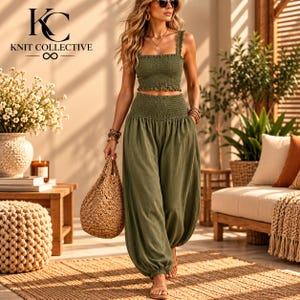 May include: An olive green two-piece set consisting of a smocked crop top with wide straps and matching high-waisted, loose-fitting trousers with a smocked waistband. The outfit is paired with a woven straw handbag.