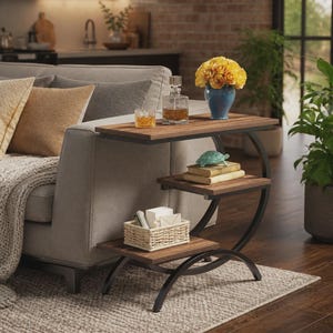 Puede incluir: Una mesa auxiliar de tres niveles con un marco de metal negro curvado y tres estantes rectangulares de madera. El estante superior sostiene un decantador de vidrio y un vaso con líquido ámbar, el medio dos libros y una figura de tortuga, y el inferior una cesta tejida.