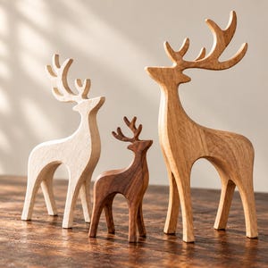 May include: Three standing deer figurines carved from wood. The left deer is light-toned, the centre deer is dark brown, and the right deer is medium-toned. Each deer features smooth, curved bodies and detailed antlers, standing upright on four legs.