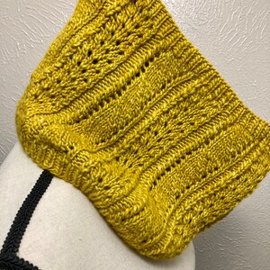May include: A yellow knitted cowl with a cable stitch pattern.