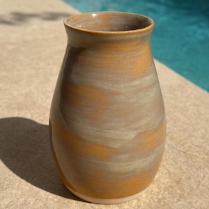 Peut inclure: Un vase en céramique à la silhouette lisse et arrondie, présentant un émail mélangé dans des tons jaune moutarde chaud et gris doux. Le récipient possède une large ouverture qui se rétrécit vers la base, finie dans un blanc cassé net.