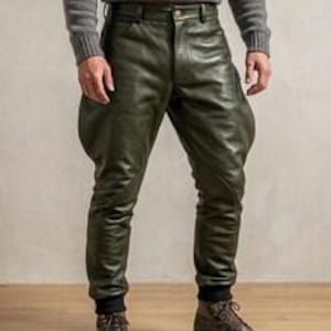 Könnte beinhalten: Olivgrüne Lederreithose mit hoher Taille, Knopfverschluss, ausgestellten Oberschenkelpartien und eng anliegenden Unterschenkeln, die in schwarzen Rippbündchen enden. Die Hose wird mit braunen Schnürstiefeln aus Leder kombiniert.