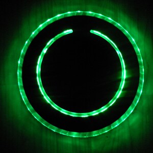 May include: A circular, black, framed object with a green LED light ring around the perimeter.