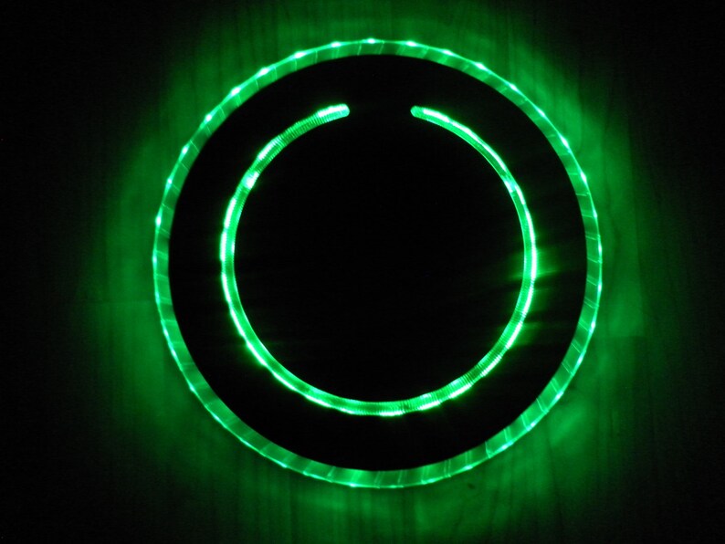 May include: A circular, black, framed object with a green LED light ring around the perimeter.