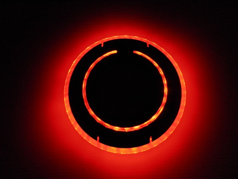 May include: A red glowing ring with a black center. The ring is made of a clear material and has a smooth surface.