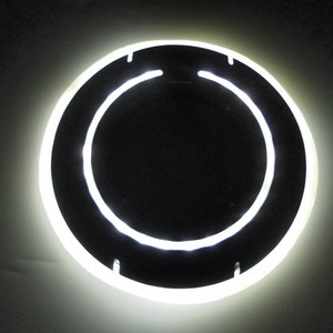 May include: A white neon ring light with a black center, mounted on a wall.