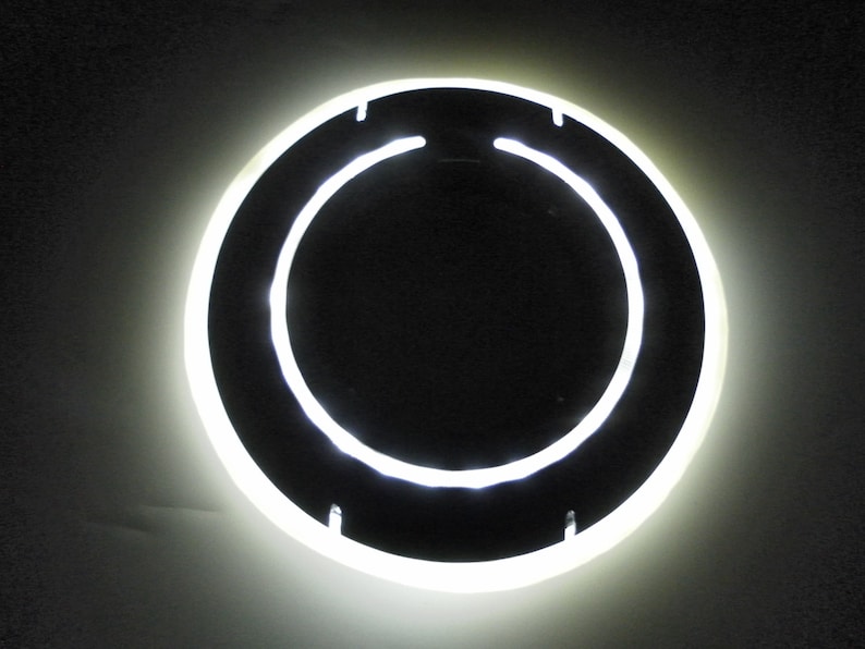 May include: A white neon ring light with a black center, mounted on a wall.