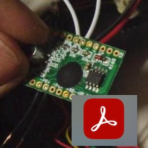 May include: A green circuit board with various electronic components, including a black circular element and several small rectangular chips. The board has gold-colored connection points and is partially obscured by a hand. A red Adobe Acrobat icon is in the corner.