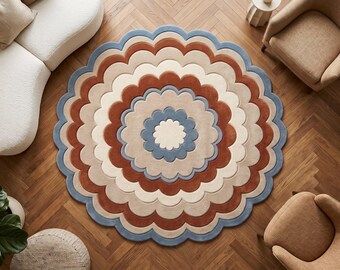 Puede incluir: Una alfombra redonda con borde festoneado y un patrón floral concéntrico. El diseño consta de anillos alternos en tonos crema, azul polvoriento y naranja terracota, creando una apariencia de capas en forma de pétalos sobre el suelo.