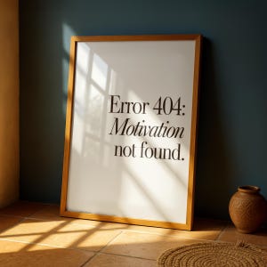 Könnte beinhalten: Ein rechteckiges gerahmtes Wandbild mit weißem Hintergrund und schwarzem Text, der Error 404: Motivation not found lautet. Der Rahmen besteht aus hellem Holz und steht aufrecht. Das Design ist schlicht, klar und modern gestaltet.