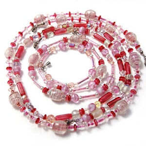 May include: A multi-strand necklace made of pink and red glass beads. The beads are of various shapes and sizes, including round, oval, and cylindrical. The necklace is strung on a silver chain.