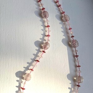May include: A pink and clear glass beaded necklace with a silver clasp. The beads are various sizes and shapes, with some having a textured surface.