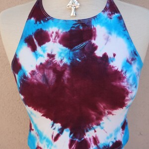 Puede incluir: Un top halter de te&ntilde;ido anudado en tonos de blanco, azul y burdeos. El top es corto y tiene un ajuste holgado. Un colgante de plata en forma de hongo cuelga de un collar gargantilla negro.