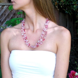 May include: A woman wearing a white strapless top with a layered pink and white beaded necklace.