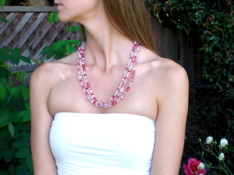 May include: A woman wearing a white strapless top with a layered pink and white beaded necklace.