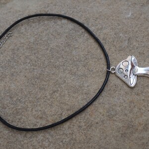 Puede incluir: Un collar de cord&oacute;n de cuero negro con un colgante de hongo plateado.