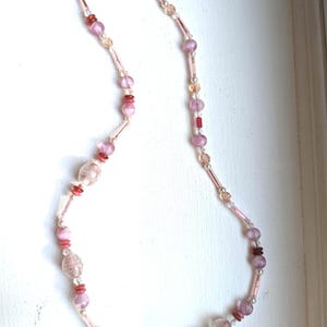 May include: A pink and red glass bead necklace with a silver clasp. The beads are various shapes and sizes, including round, oval, and rectangular.