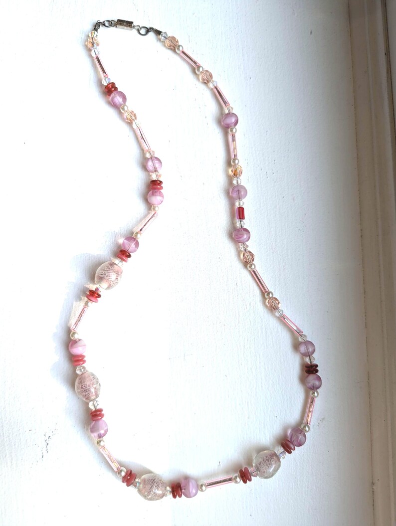 May include: A pink and red glass bead necklace with a silver clasp. The beads are various shapes and sizes, including round, oval, and rectangular.