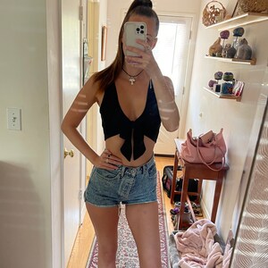 Puede incluir: Una mujer con un top corto negro con un lazo y pantalones cortos de mezclilla de cintura alta.