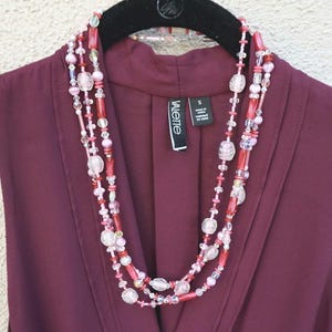 May include: A multi-strand necklace with pink, red, and clear beads. The necklace is layered and has a variety of bead shapes and sizes.